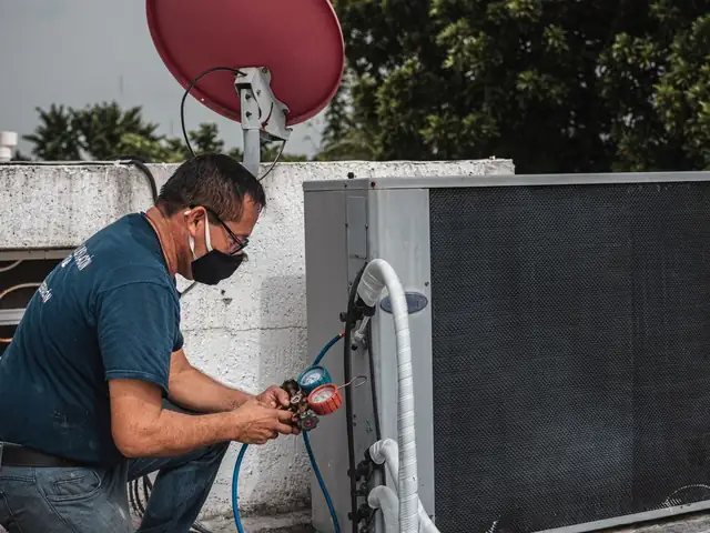 Technician in a mask testing an outdoor air conditioning unit with gauges